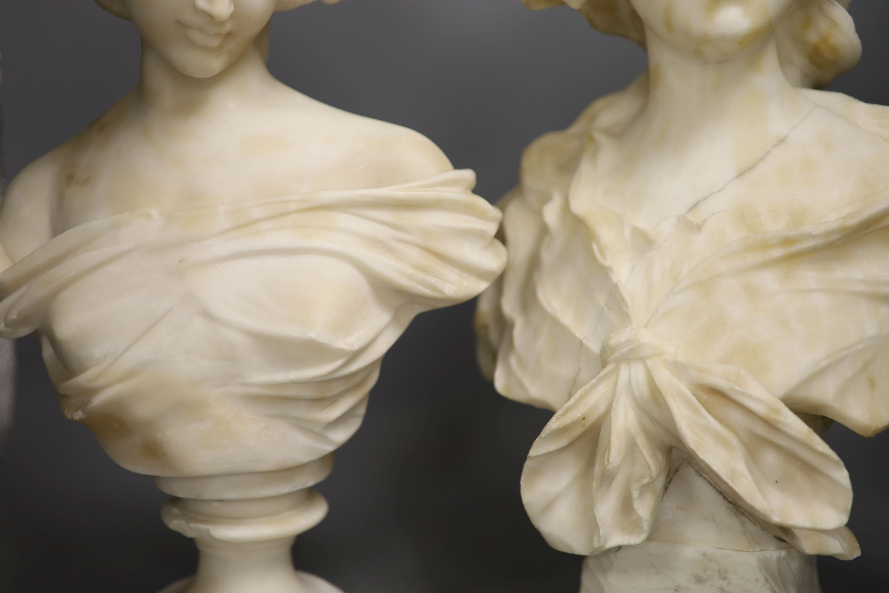 Two white alabaster busts of young women, raised on turned plinths 44cm